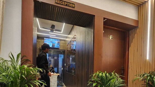 A reception area with a sign, a man standing, and potted plants. - The Trishul Stay (Varanasi)