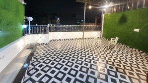 A rooftop terrace with a geometric patterned floor, green artificial grass walls, and a metal railing. - The Trishul Stay (Varanasi)