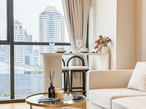 A modern living room with a sofa, a round glass coffee table, a chair, and a view of a cityscape through large windows. - Luxe City Condo in Central Bangkok · (Bangkok)