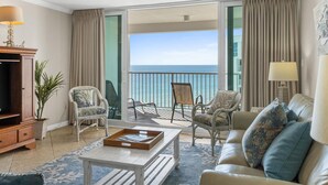 Ein Hotelzimmer mit Balkon, einer Couch, zwei Sesseln, einem Couchtisch und einem Fernseher.