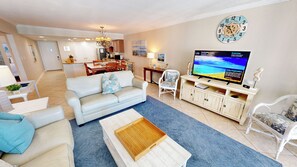A living room with a sofa, coffee table, TV, and a dining area in the background. - Open Balcony w/Amazing Views ST 1115 with Beach Svc for 2 included (Destin)