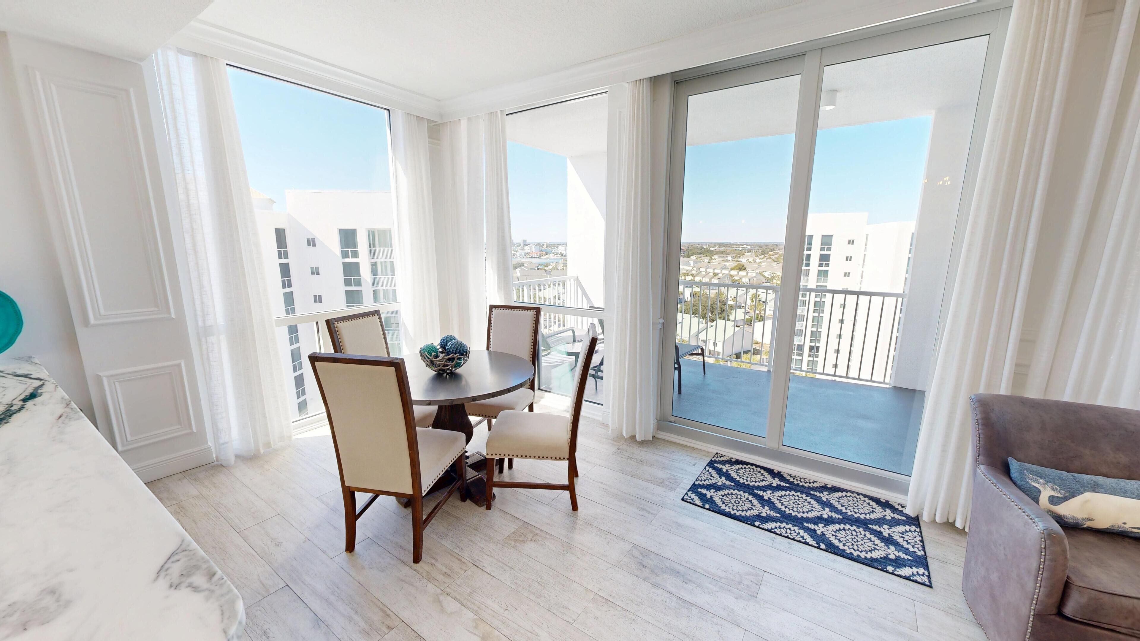 Ein Balkon mit Esstisch und Stühlen, Blick auf Gebäude, und ein blaues Teppich mit Muster.