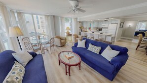 Un salon moderne avec des canapés bleus, une table basse en verre et un coin repas comprenant une table et des chaises en verre.
