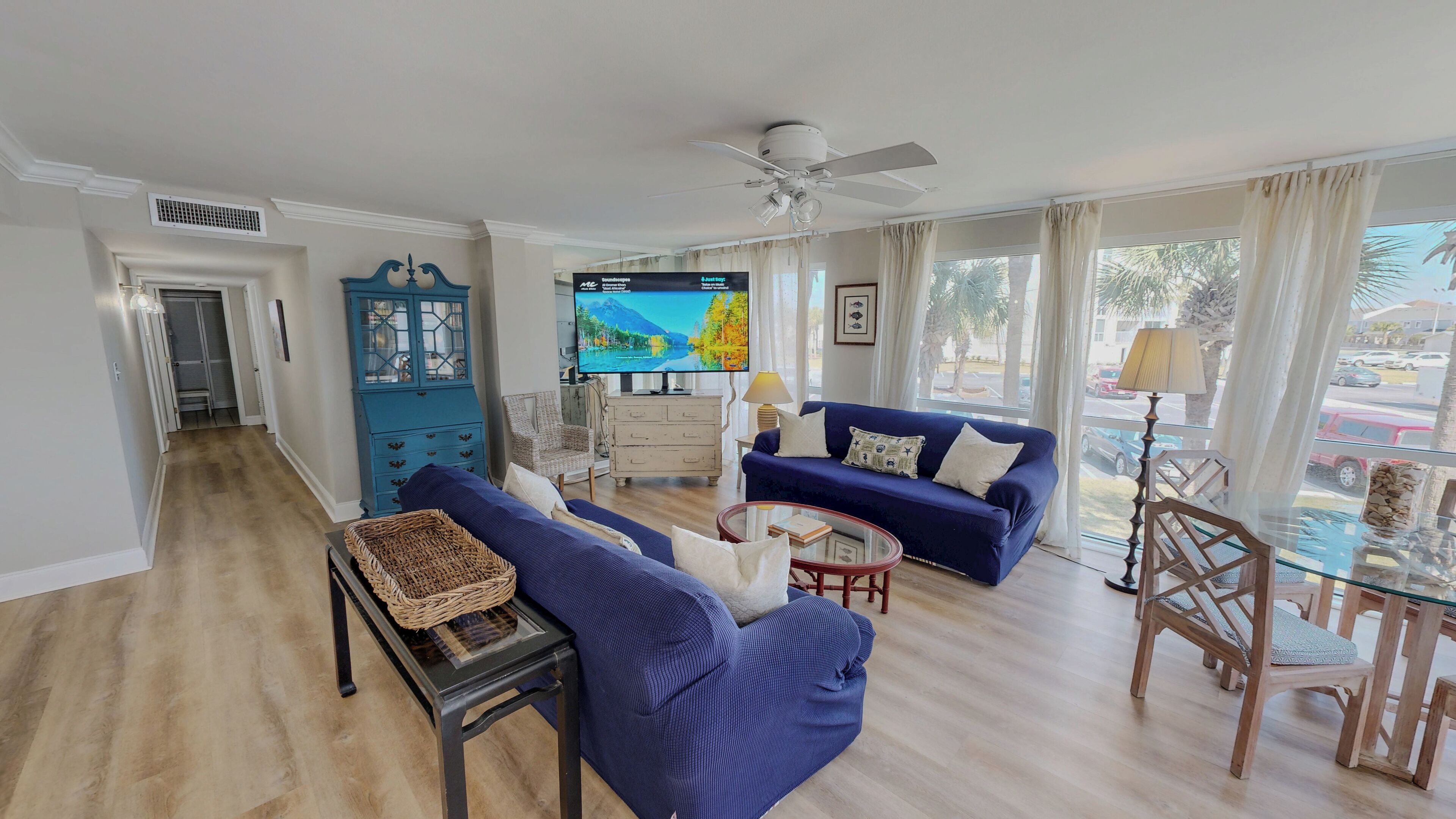 A living room with a blue sofa, a glass coffee table, a wicker basket, and a television.