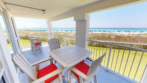 Ein Balkon mit Tisch und Stühlen, der einen Blick auf einen Strand mit Sonnenschirmen und Personen bietet.