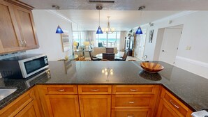 A kitchen with wooden cabinets, a microwave, a glass-top dining table, and a bowl on the counter. - Aqua Waves of Destin. Amazing Beach with Free Beach Set Up! (Destin)