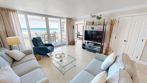 A living room with a sofa, armchair, TV, and a glass coffee table. - Aqua Waves of Destin. Amazing Beach with Free Beach Set Up! (Destin)