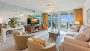A spacious living room with a television, comfortable seating, a balcony with a view of the beach, and a ceiling fan. - Perfect Beachfront Location ST 2054 (Destin)