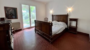 A bedroom with a wooden bed, a radiator, a desk, and a large window with a view of greenery. - Holiday Home “L'angèle - Spacious With” with Private Terrace, Wi-Fi & Air Conditioning (Portel-des-Corbières)