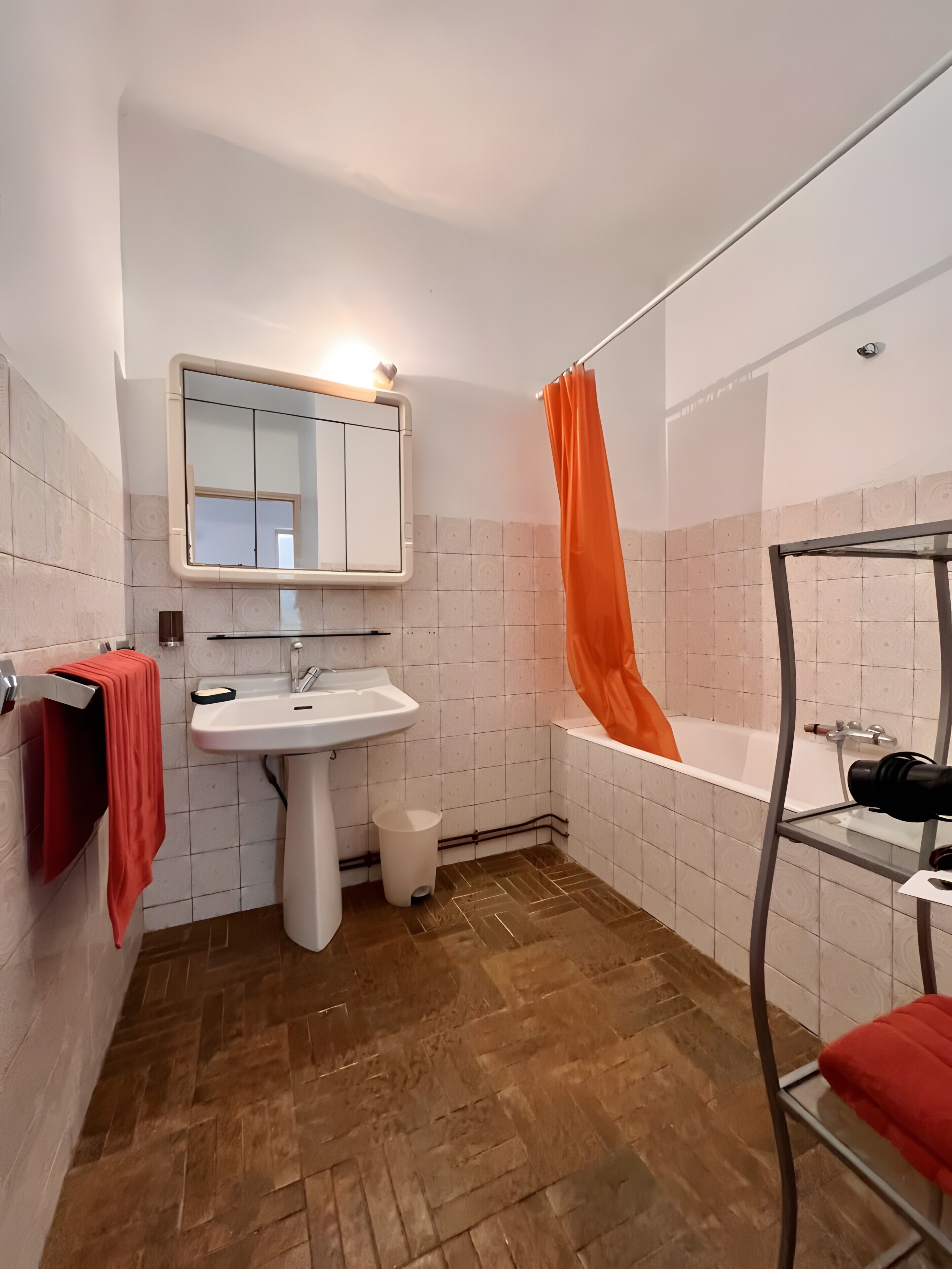 Un baño con lavabo, espejo, ducha y una toalla roja en un perchero.