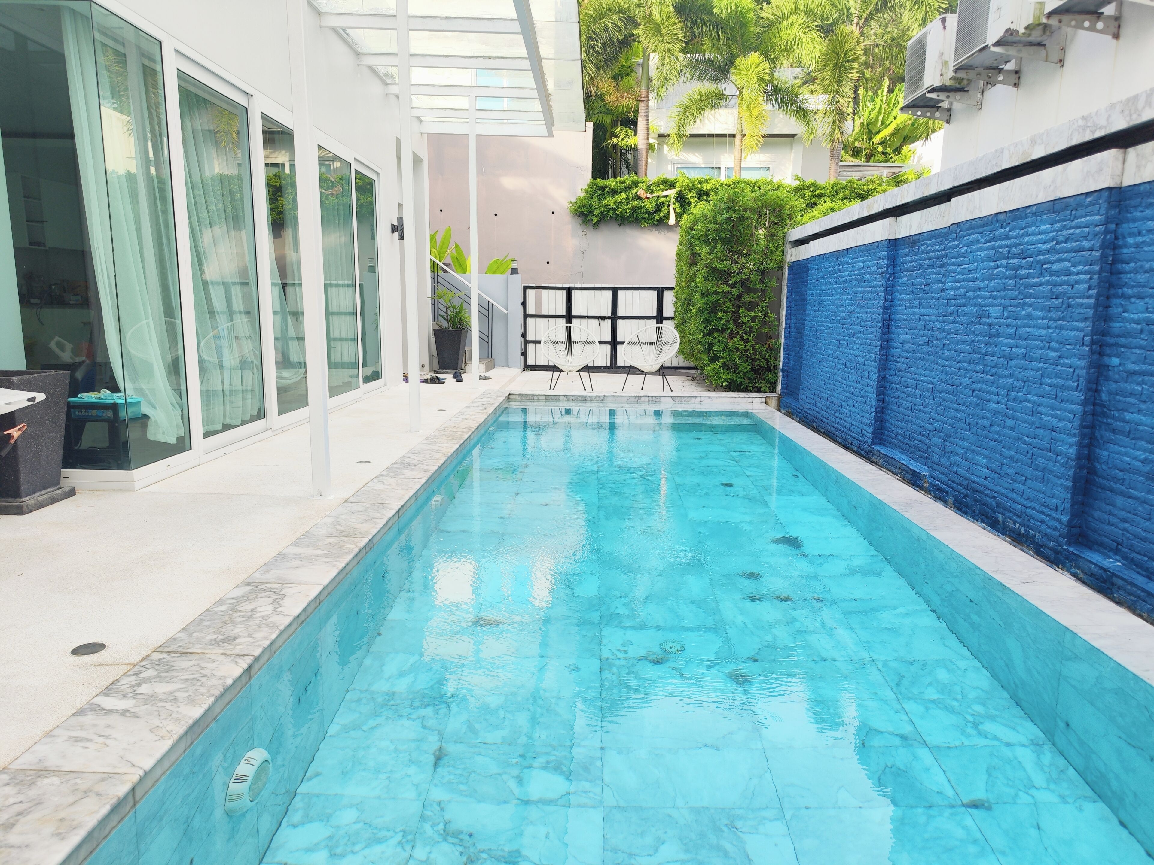 Una piscina con borde de azulejos azules, rodeada por un edificio blanco con ventanas amplias y un muro de ladrillo azul.