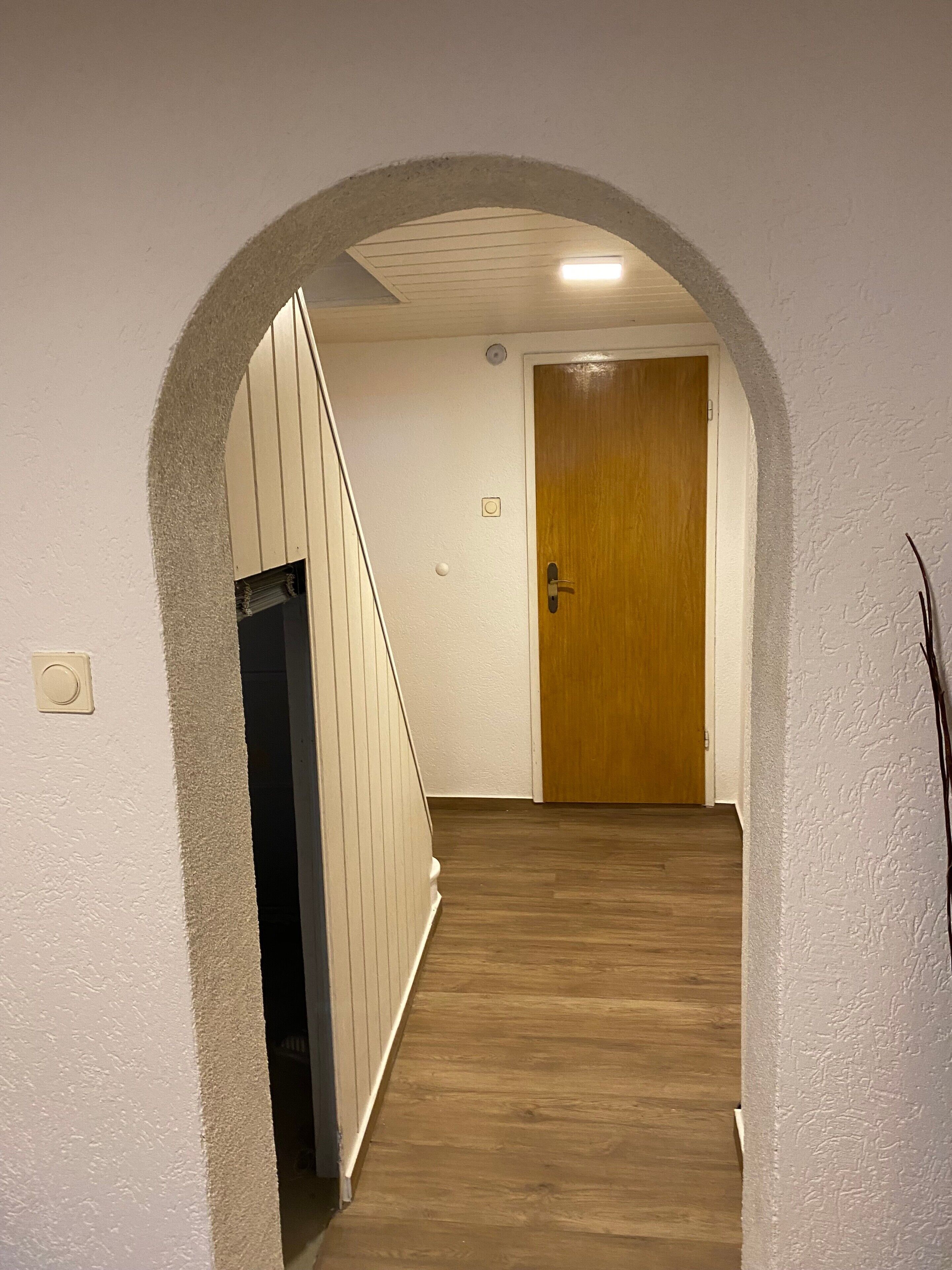 A hallway with a wooden floor, a wooden door, and a white wall.
