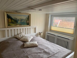 Ein Schlafzimmer mit Bett, Kissen, einem Gemälde, einem Fenster mit Jalousien und einer Heizung.