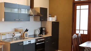 A compact kitchen with modern appliances, a dining area with a table and chairs, and a window with a view. - Apartment 'Harz Idylle 2' with Wi-Fi (Güntersberge)