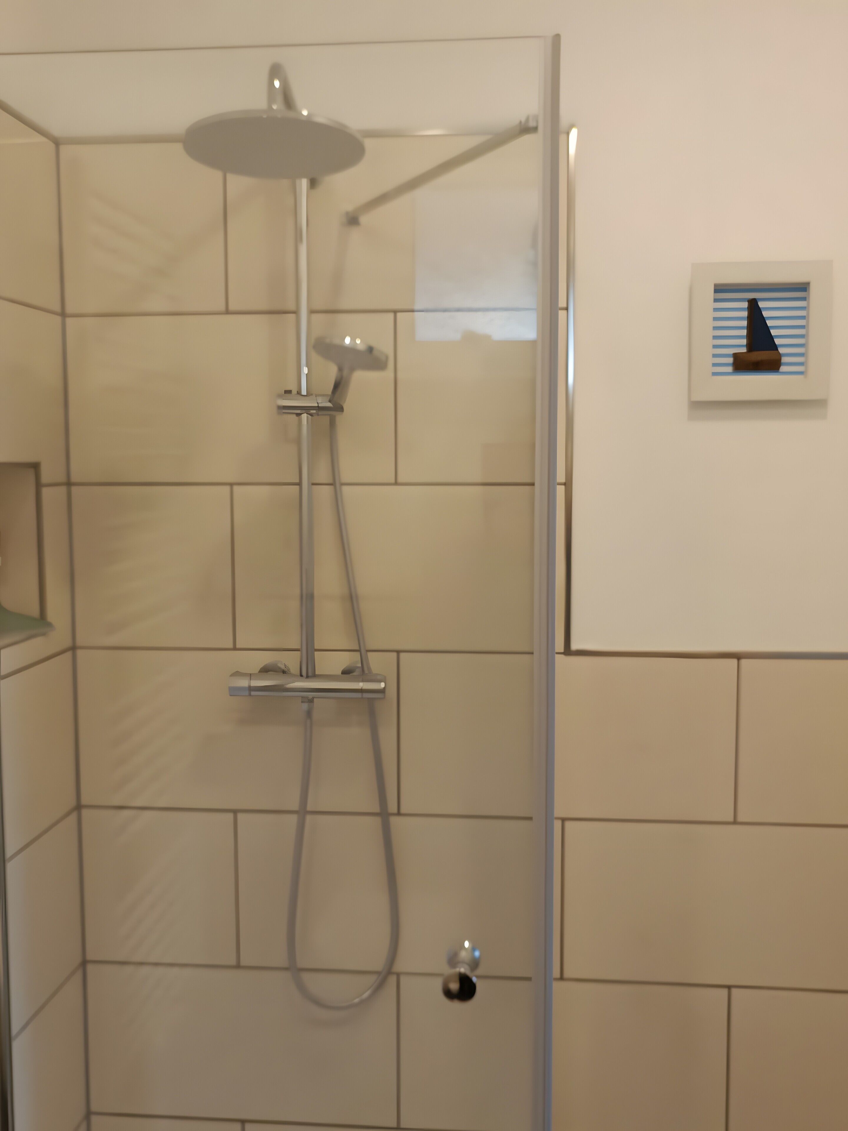 Une douche avec une porte en verre, un pommeau de douche amovible et un panneau de commande fixé au mur.