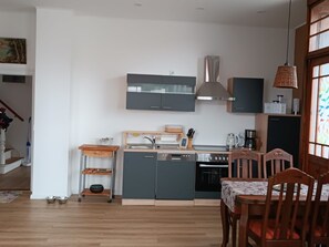 Uma cozinha moderna com armários cinza, forno embutido e área de refeições com cadeiras de madeira.