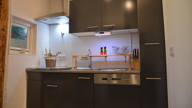 Une cuisine moderne avec des meubles de couleur sombre, un lave-vaisselle et une étagère en bois où sont rangés les ustensiles de cuisine.