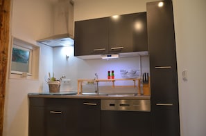 Uma cozinha moderna com armários escuros, lava-louças e uma prateleira de madeira com utensílios de cozinha.