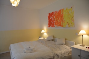 Quarto de hotel com cama, mesas de cabeceira, luminárias e um quadro abstrato grande na parede.