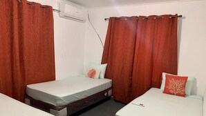 A room with two beds, each with a mattress and pillow. There is a window with curtains, and an air conditioning unit on the wall.