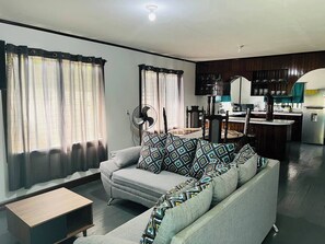 Un salon comprenant un canapé, une table basse et un ventilateur. Il y a également un coin cuisine avec une cuisinière et des placards.