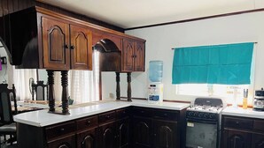 A kitchen with dark wooden cabinets, a white countertop, a built-in oven, and a window with a teal curtain.