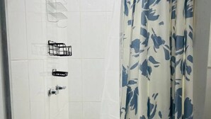 A shower area with a glass door, a showerhead, and a floral curtain.