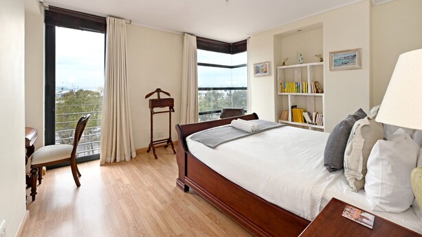 Un dormitorio con una cama grande, un escritorio, una silla, una estantería y una ventana con cortinas.