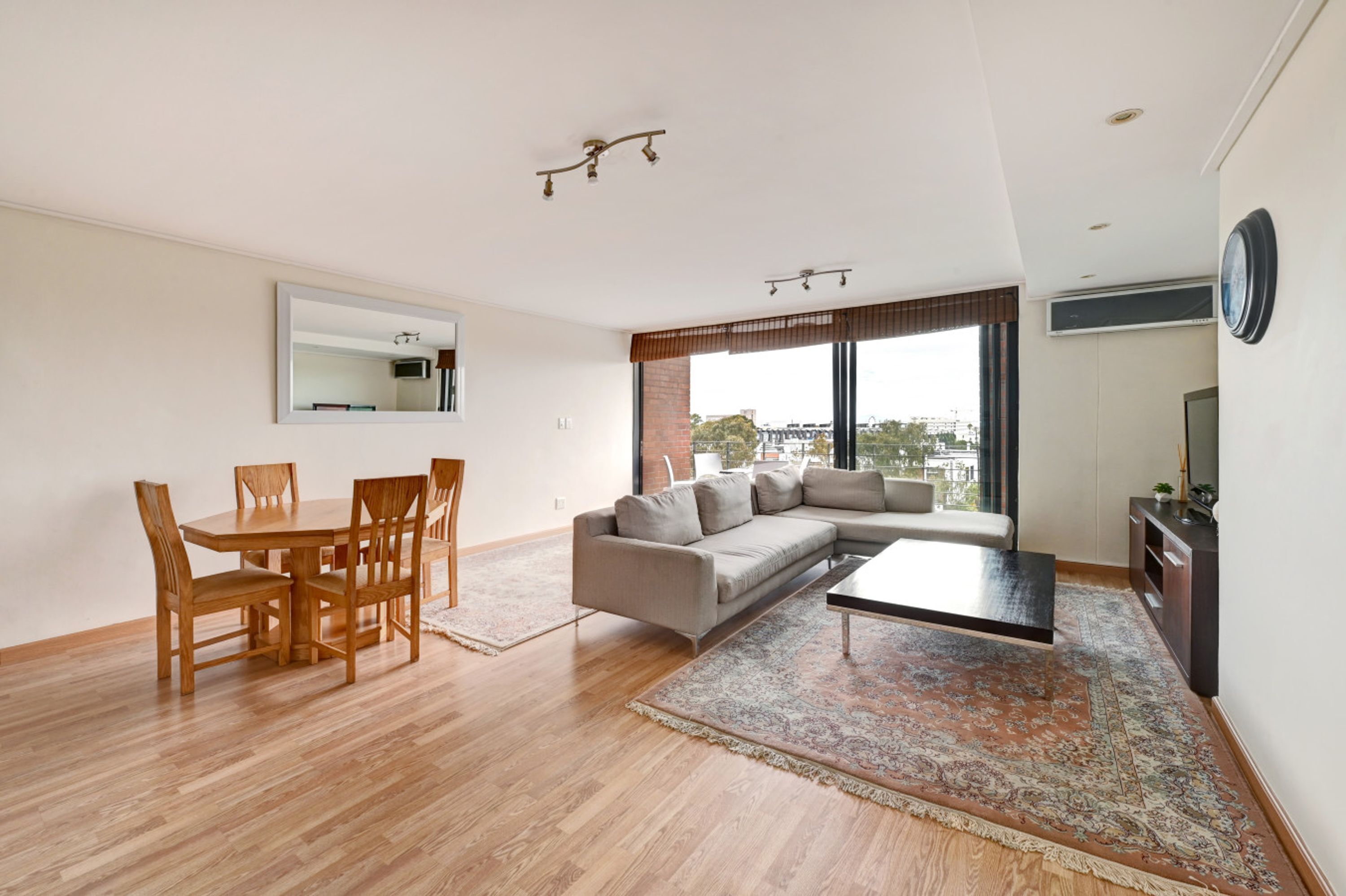 Una sala moderna con una mesa de comedor de madera, un sofá color beige y un ventanal con vista a la ciudad.