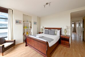 A neatly arranged bedroom with a wooden bed, bedside tables, a bookshelf, and a chair. - Two Bed | Spacious | 6th Floor | Secure (Cape Town)