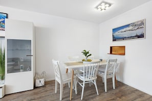 Ein Essbereich mit Tisch, Stühlen, einer Topfpflanze und einem gerahmten Bild an der Wand.