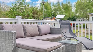 Un espace de détente extérieur aménagé avec des meubles en osier, comprenant un canapé rembourré et une table à plateau en verre, le tout entouré d’une clôture blanche.