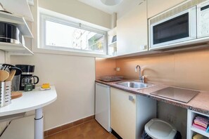 Eine kompakte Küche mit Mikrowelle, Spüle und kleinem Geschirrspüler. Ein Fenster sorgt für natürliches Licht, und eine weiße Arbeitsplatte mit diversen Küchenutensilien.
