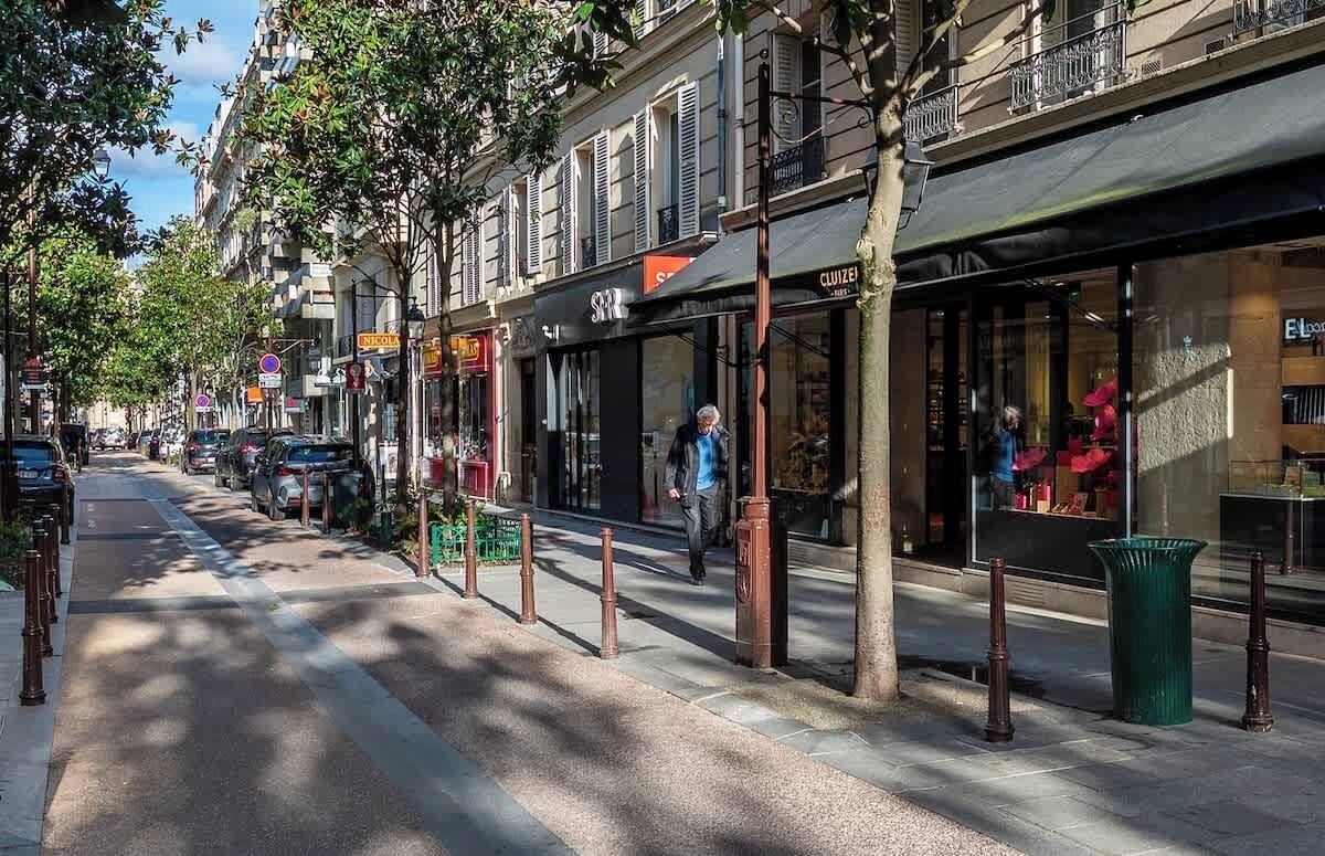 A street with storefronts, a pedestrian, and a parked car.