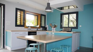 Een moderne keuken met een groot eiland, blauwe stoelen en uitzicht op groen.