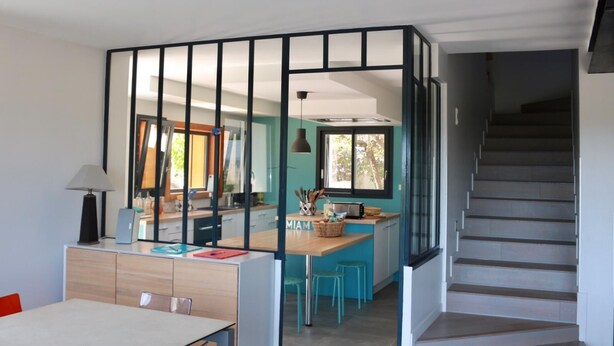Een moderne keuken met een centraal eiland, een eethoek met tafel en stoelen, en een trap die naar een hoger gelegen verdieping leidt.