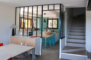 A modern kitchen with a central island, a dining area with a table and chairs, and a staircase leading to an upper level. - House - South Ardèche - sleeps 10 - private pool, panoramic view and large garden (Bourg-Saint-Andéol)