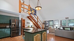 A spacious kitchen with a central island, wooden staircase, and a living area with a sofa and a large window. - Colt Mountain Lodge. (Bozeman)
