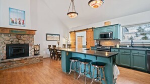 A spacious kitchen with a stone fireplace, teal bar stools, and a large island. - Colt Mountain Lodge. (Bozeman)