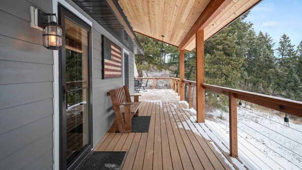 A wooden deck with a bench and a flag, leading to a covered porch with a view of a snowy landscape. - Colt Mountain Lodge. (Bozeman)