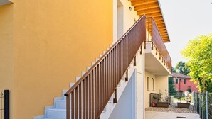Un bâtiment moderne à la façade jaune, doté d’un escalier en béton avec des rampes en bois et d’un espace extérieur couvert.