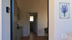 Un couloir étroit au plancher de bois menant à une cuisine équipée d’un évier et de placards.