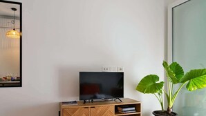A modern bedroom with a wooden cabinet, a flat-screen TV, a large window, and a potted plant. - Garden Terrace Apartment w/ A/C & Parking (San Stino di Livenza)