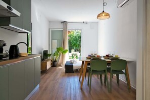 A modern kitchen with a dining area, wooden flooring, and a view of greenery outside. - Appartamento papavero (San Stino di Livenza)