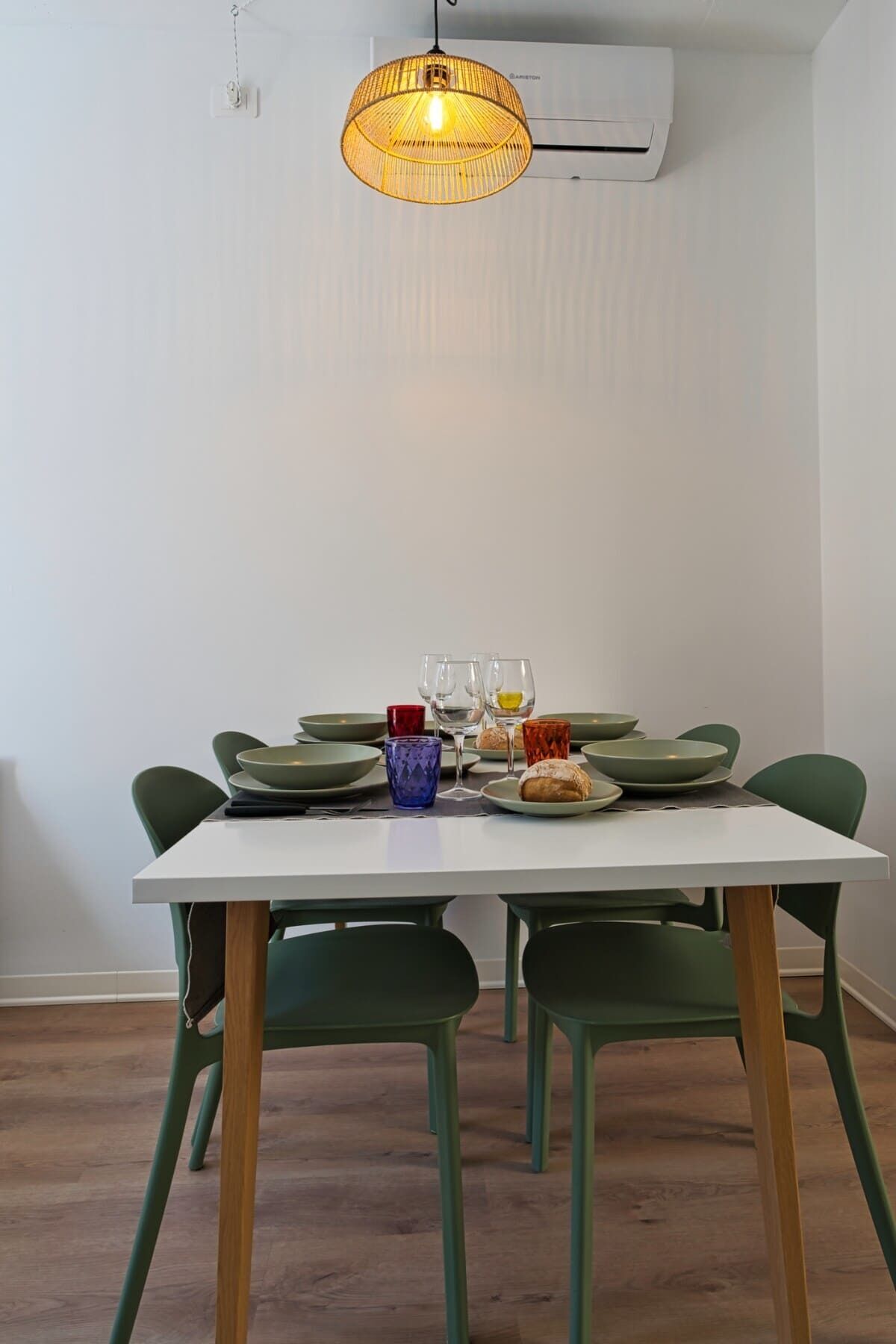 Un comedor con una mesa blanca, sillas verdes y una lámpara colgante.