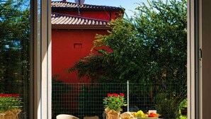 A patio area with a table set for two, outdoor chairs, and a view of a red building with a tiled roof. - Garden Terrace Apartment w/ A/C & Parking (San Stino di Livenza)