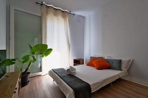 A bedroom with a bed, a bedside table, a potted plant, and a window with curtains. - Appartamento papavero (San Stino di Livenza)