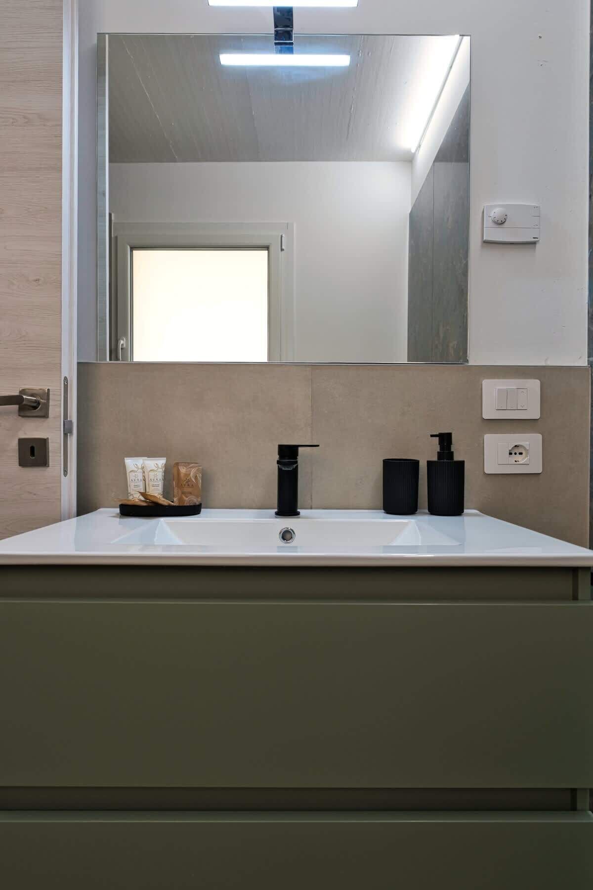 A modern bathroom with a large mirror, a white sink, and two black soap dispensers.