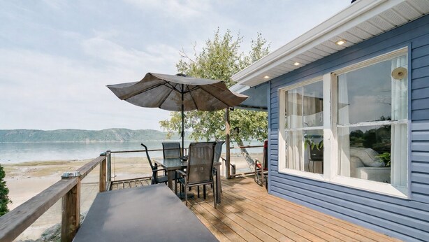 Una terraza de madera con una mesa y sillas, con vista a una playa y al agua.