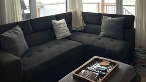 Una sala de estar moderna con un sofá seccional gris oscuro, una mesa de centro de madera con juegos de mesa y ventanas grandes que ofrecen vistas de un paisaje nevado.